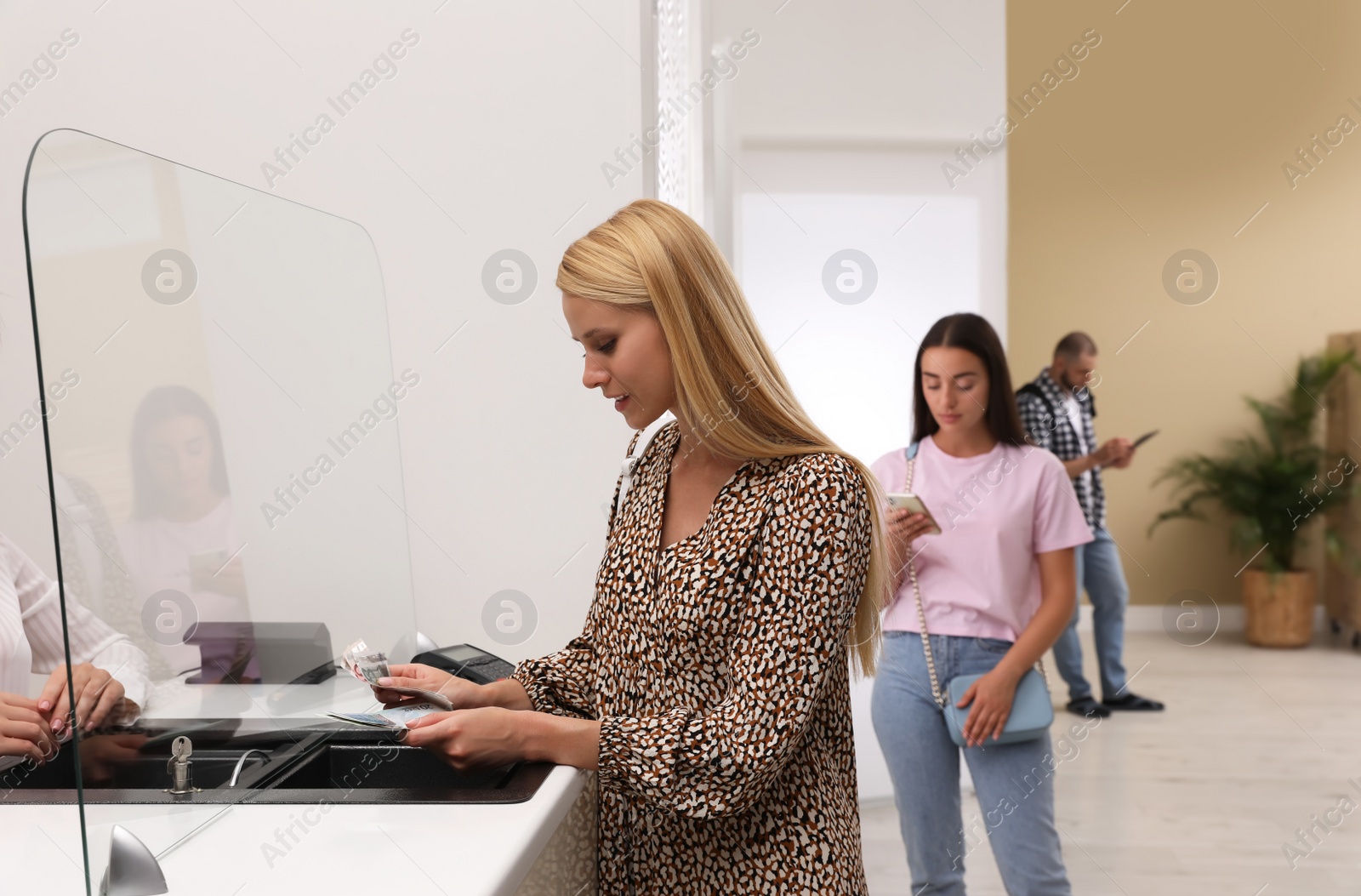 Photo of Woman with money and other people in line at cash department window. Currency exchange