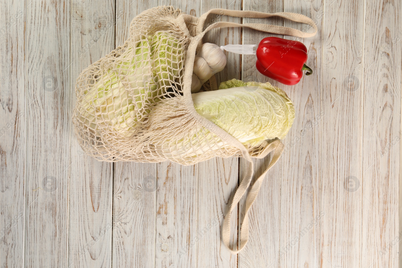 Photo of Fresh Chinese cabbage, bell pepper and garlic in net bag on wooden table, top view