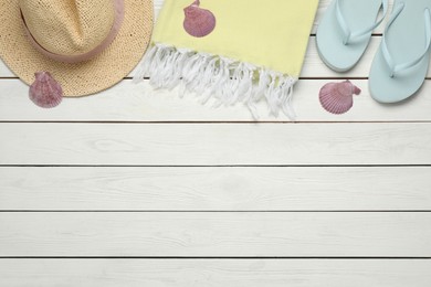 Beach towel, straw hat and flip flops on white wooden background, flat lay. Space for text