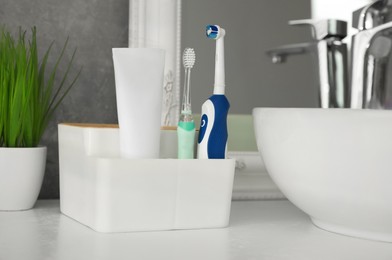 Photo of Electric toothbrushes and tube of paste near vessel sink on countertop in bathroom, closeup