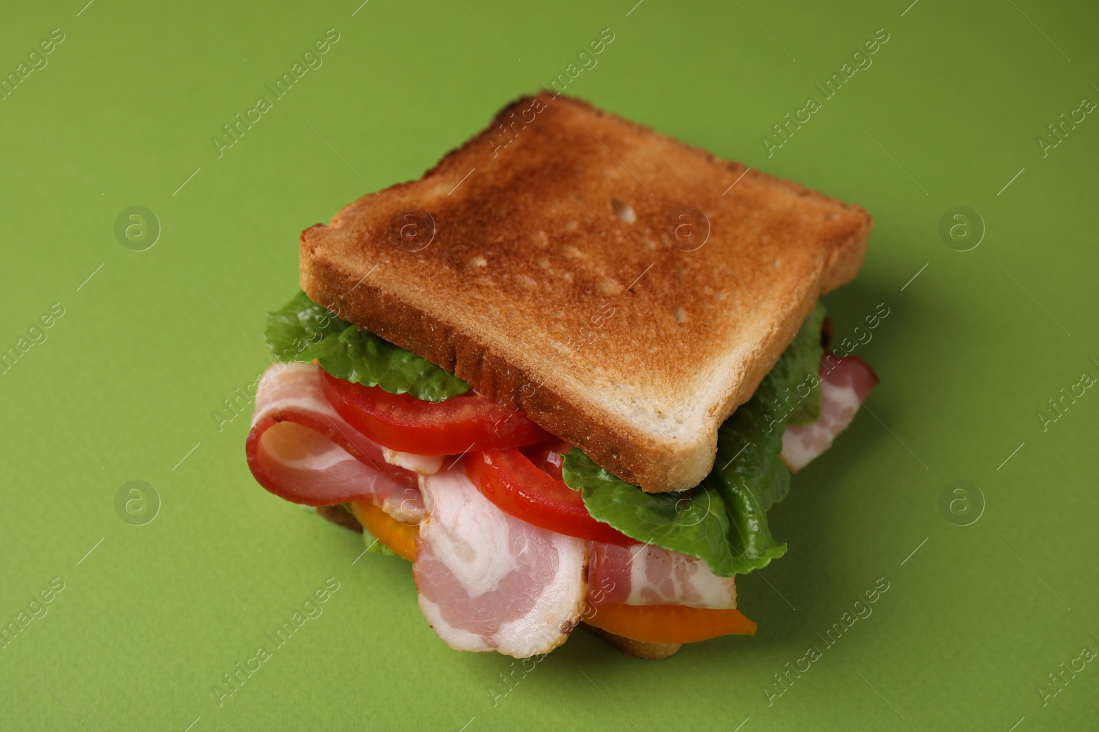 Photo of Tasty sandwich with bacon and tomato on green table