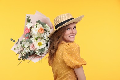 Happy woman in straw hat with bouquet of beautiful flowers on yellow background