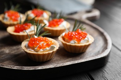 Delicious tartlets with red caviar and cream cheese served on wooden table, closeup