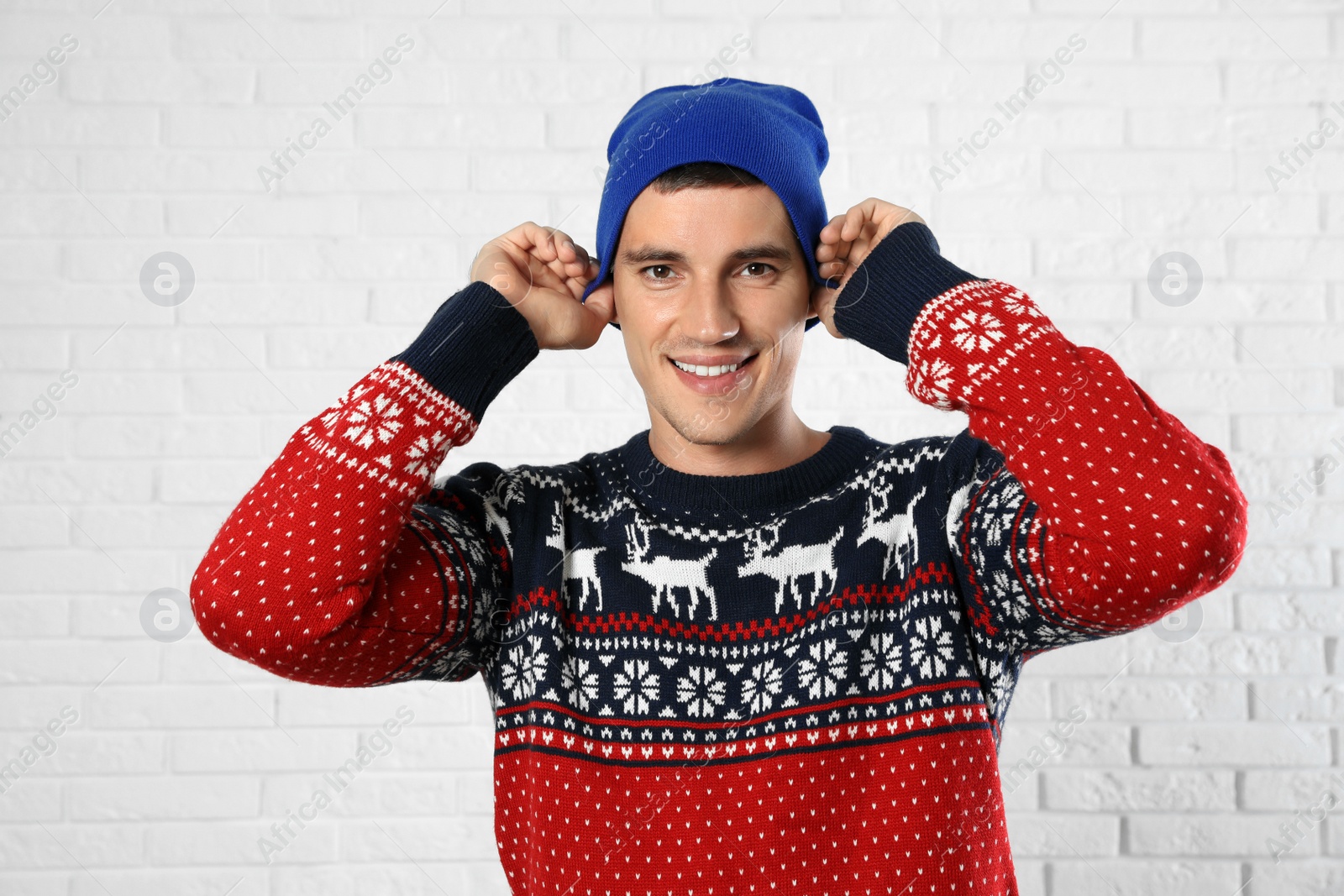 Photo of Portrait of young man in Christmas sweater and hat near white brick wall