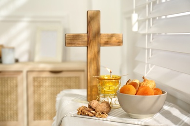 Photo of Dried fruits, walnuts, candle and wooden cross on window sill indoors. Great Lent season