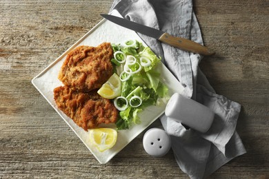 Photo of Tasty schnitzels served with lemon and salad on wooden table, flat lay