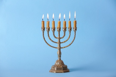 Photo of Golden menorah with burning candles on light blue background