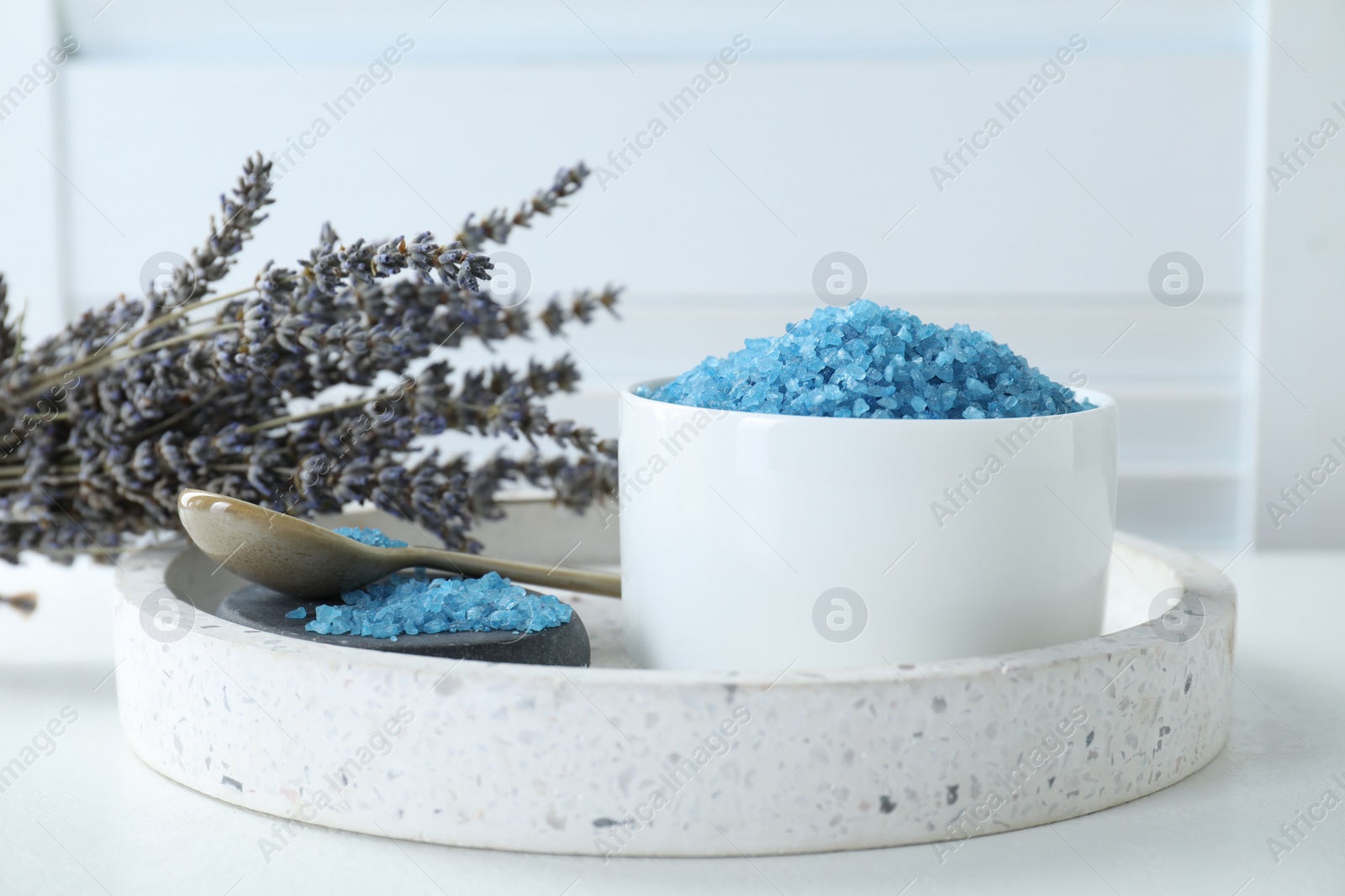 Photo of Bowl with blue sea salt and lavender flowers on white table indoors
