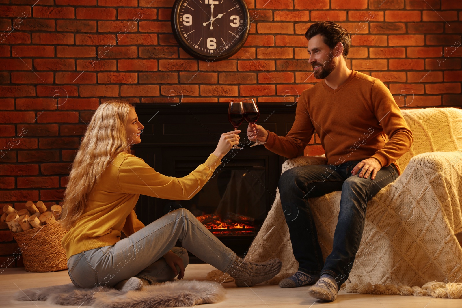 Photo of Lovely couple with glasses of wine spending time together near fireplace at home
