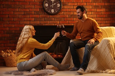 Photo of Lovely couple with glasseswine spending time together near fireplace at home