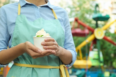 Woman holding cup with tasty frozen yogurt outdoors, closeup. Space for text