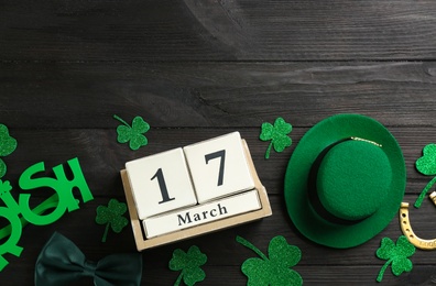 Photo of Leprechaun's hat, block calendar and St. Patrick's day decor on black wooden background, flat lay. Space for text