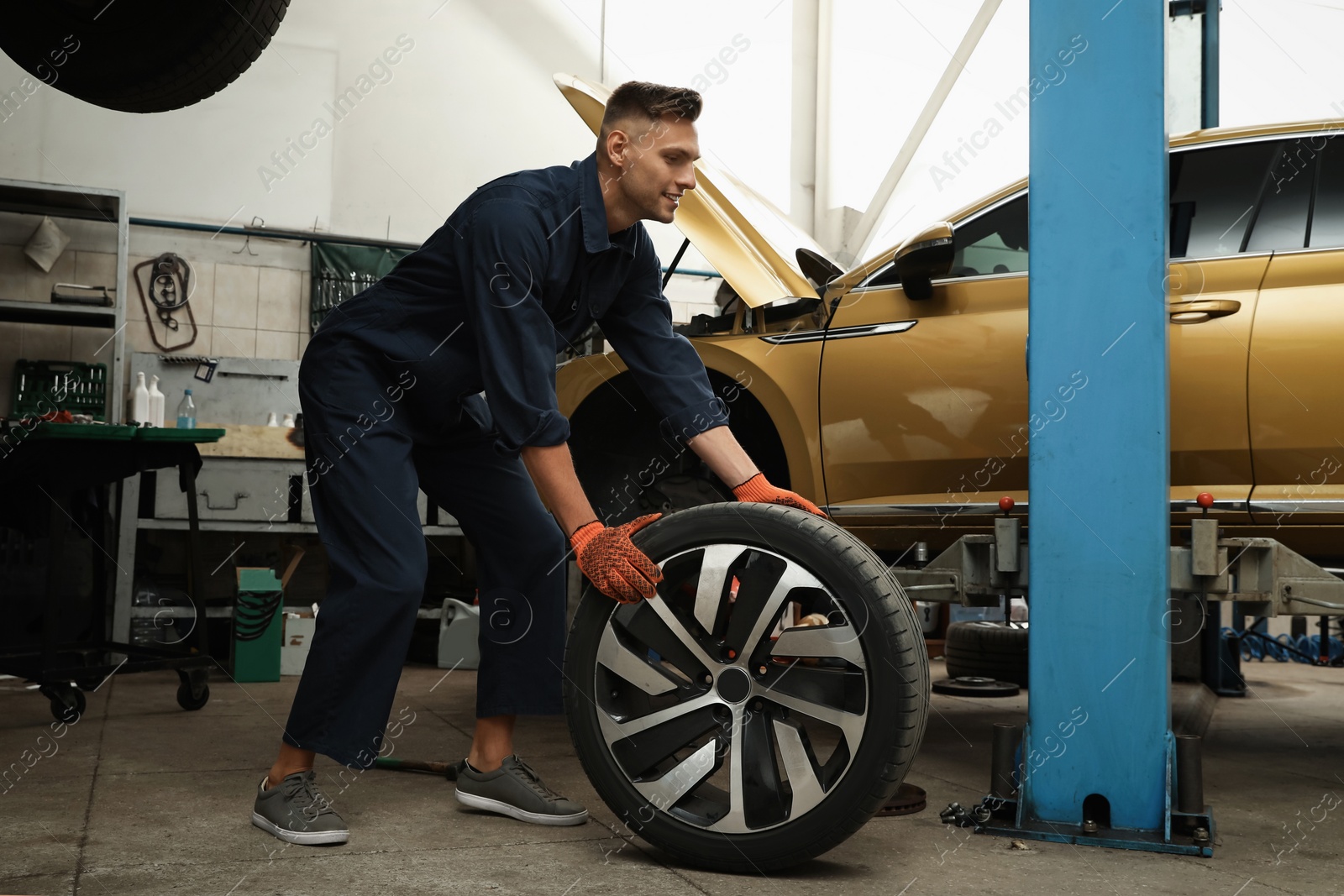 Photo of Professional mechanic with car wheel at automobile repair shop