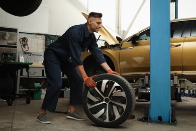 Professional mechanic with car wheel at automobile repair shop