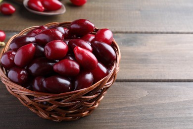 Photo of Fresh ripe dogwood berries in wicker bowl on wooden table, closeup. Space for text