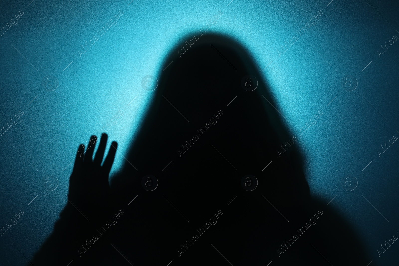 Photo of Silhouette of ghost behind glass against blue background