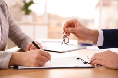 Photo of Real estate agent giving key with trinket to client in office, closeup