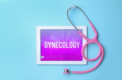 Tablet with word GYNECOLOGY and stethoscope on light blue background, flat lay