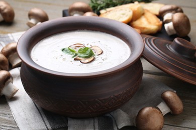 Photo of Delicious homemade mushroom soup in ceramic pot and fresh ingredients on wooden table