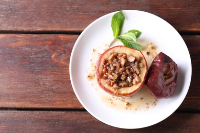 Photo of Tasty baked apple with nuts, honey and mint on wooden table, top view. Space for text