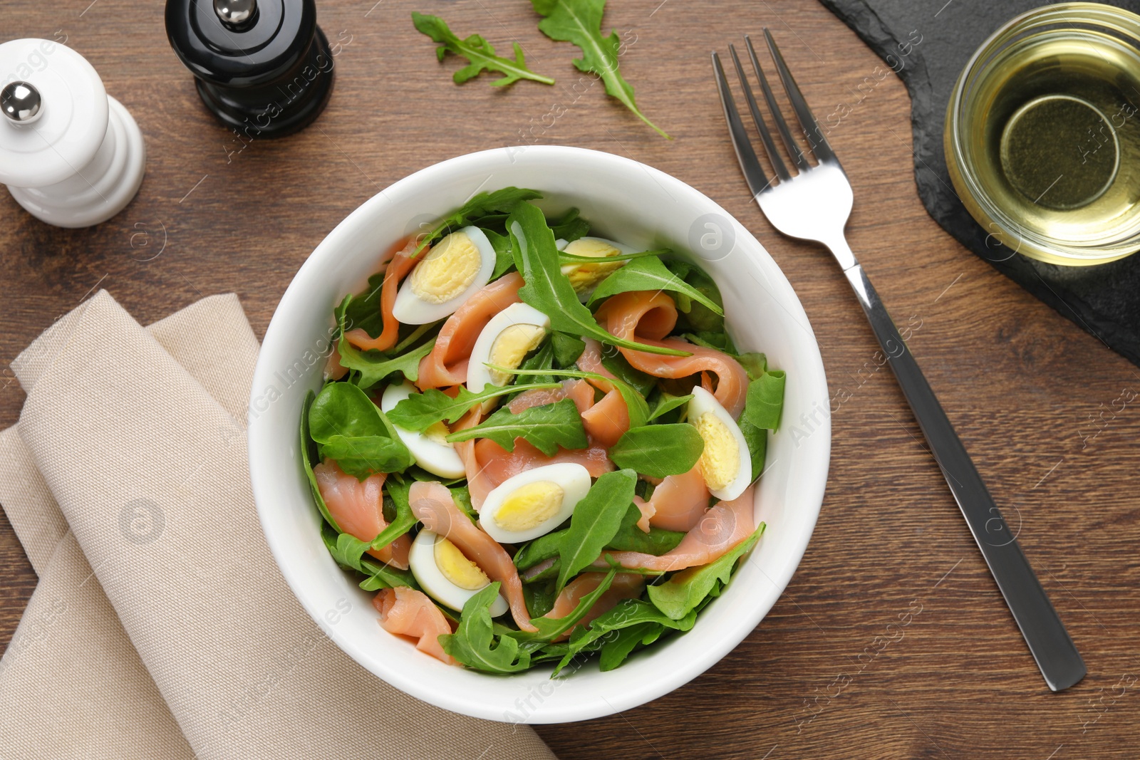 Photo of Delicious salad with boiled eggs, salmon and arugula served on wooden table, flat lay