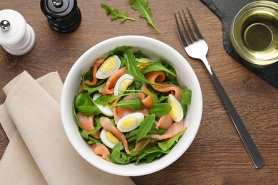 Delicious salad with boiled eggs, salmon and arugula served on wooden table, flat lay