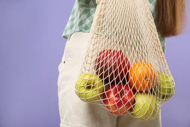 Photo of Woman with string bag of fresh fruits on violet background, closeup