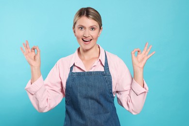 Photo of Beautiful young woman in denim apron on light blue background