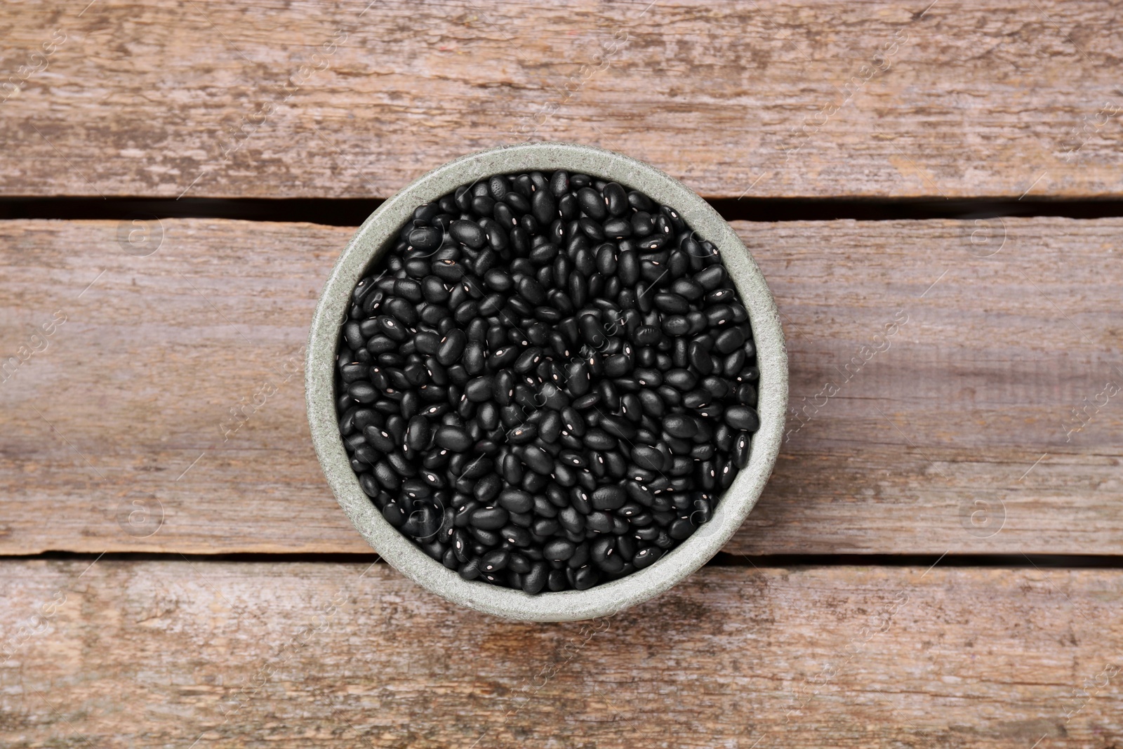 Photo of Bowl of raw black beans on wooden table, top view