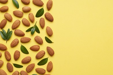 Photo of Delicious almonds and fresh leaves on yellow background, flat lay. Space for text