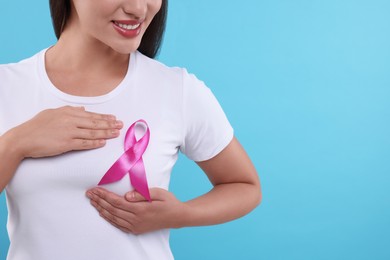 Photo of Woman with pink ribbon on light blue background, closeup and space for text. Breast cancer awareness