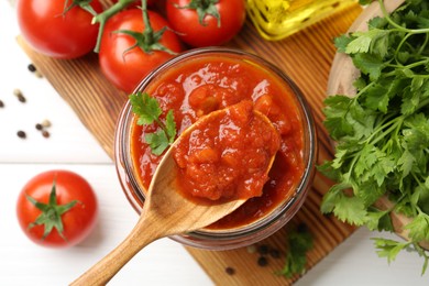 Photo of Homemade tomato sauce in jar, spoon and fresh ingredients on white wooden table, flat lay