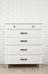 Modern chest of drawers near white brick wall