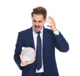 Emotional young businessman with piggy bank on white background