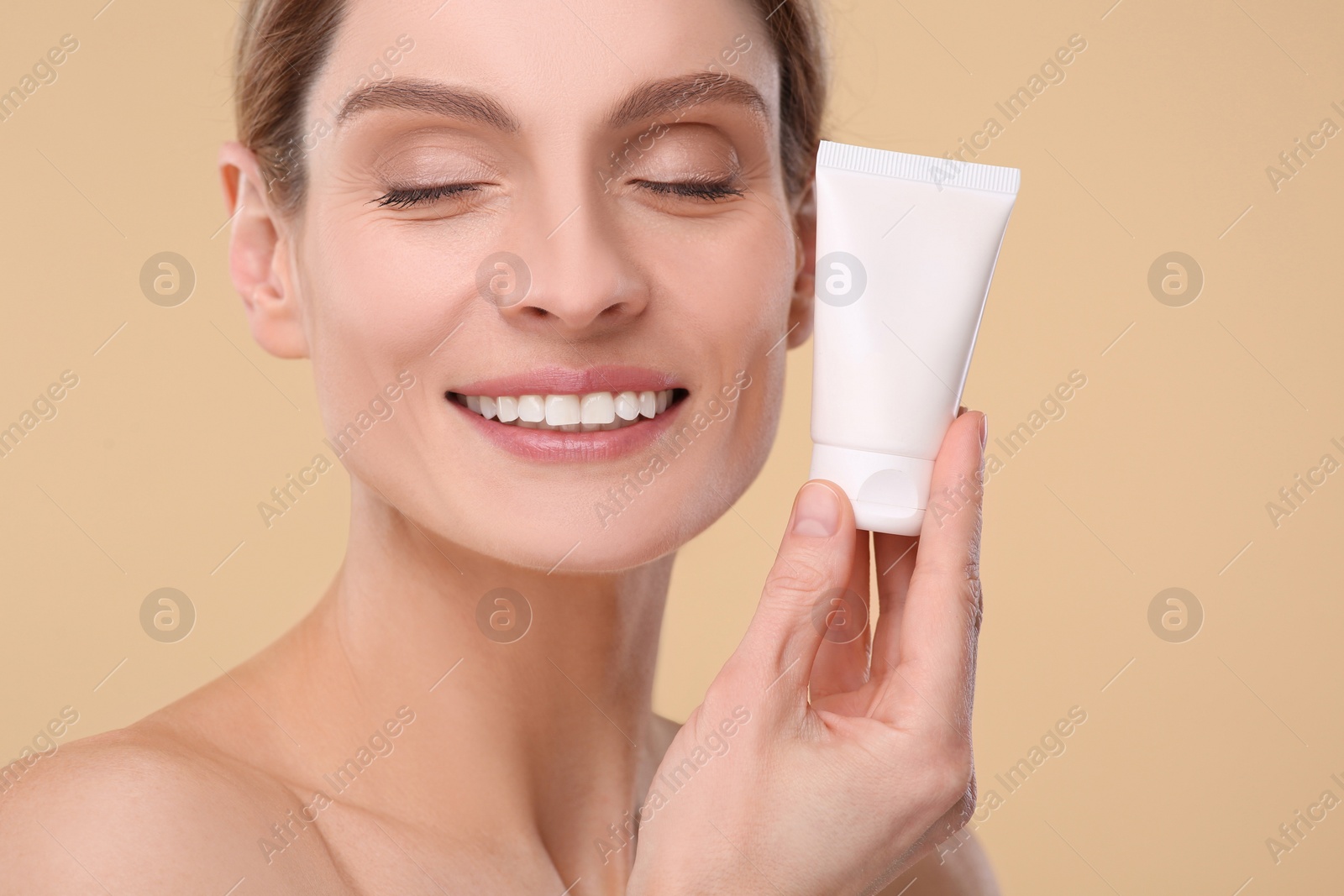 Photo of Woman holding tube of foundation on beige background