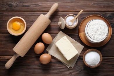 Photo of Making shortcrust pastry. Rolling pin and different ingredients for dough on wooden table, flat lay