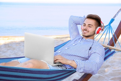 Photo of Young man listening to music in comfortable hammock at seaside