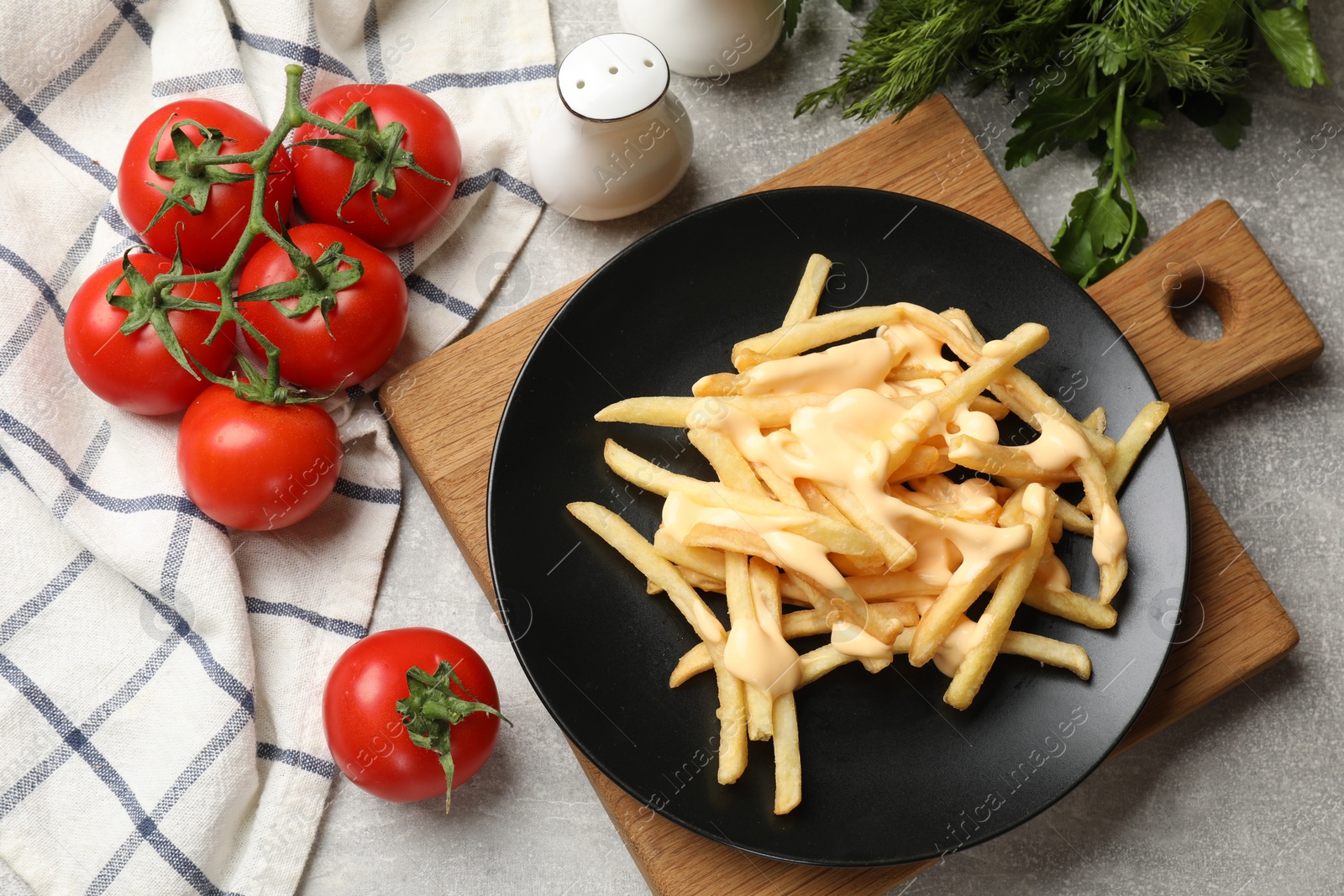 Photo of Delicious French fries with cheese sauce, tomatoes, dill and parsley on grey table, flat lay