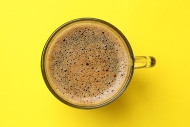 Photo of Aromatic coffee in glass cup on yellow background, top view