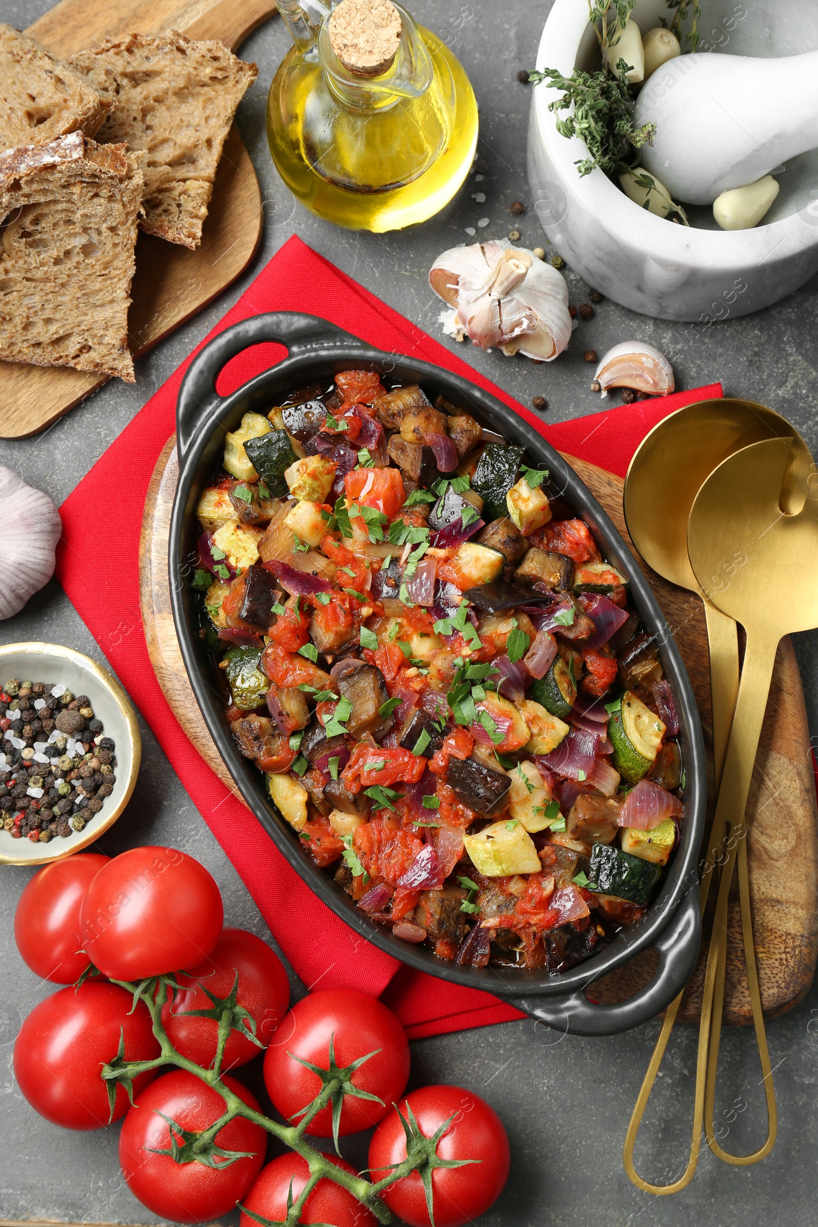 Photo of Dish with tasty ratatouille, ingredients and bread on grey textured table, flat lay