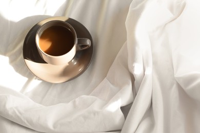 Photo of Cup of aromatic coffee on bed in morning, above view. Space for text