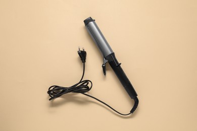 Photo of Curling iron on beige background, top view