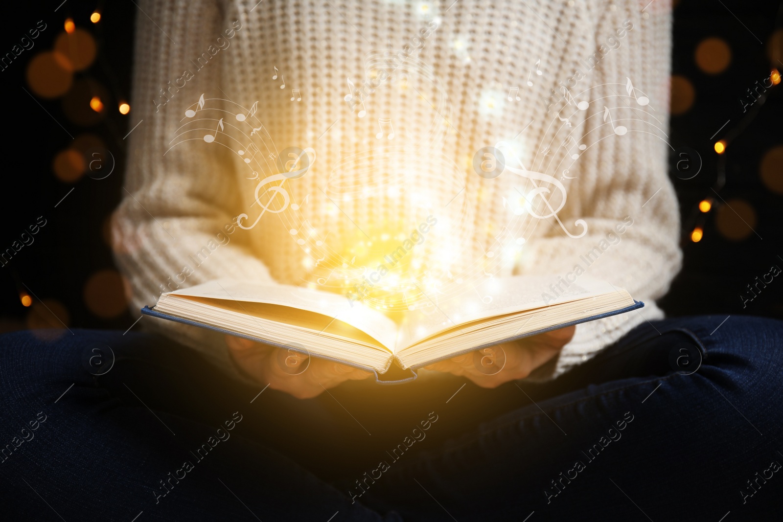 Image of Young woman holding open book with musical notes against dark background , closeup