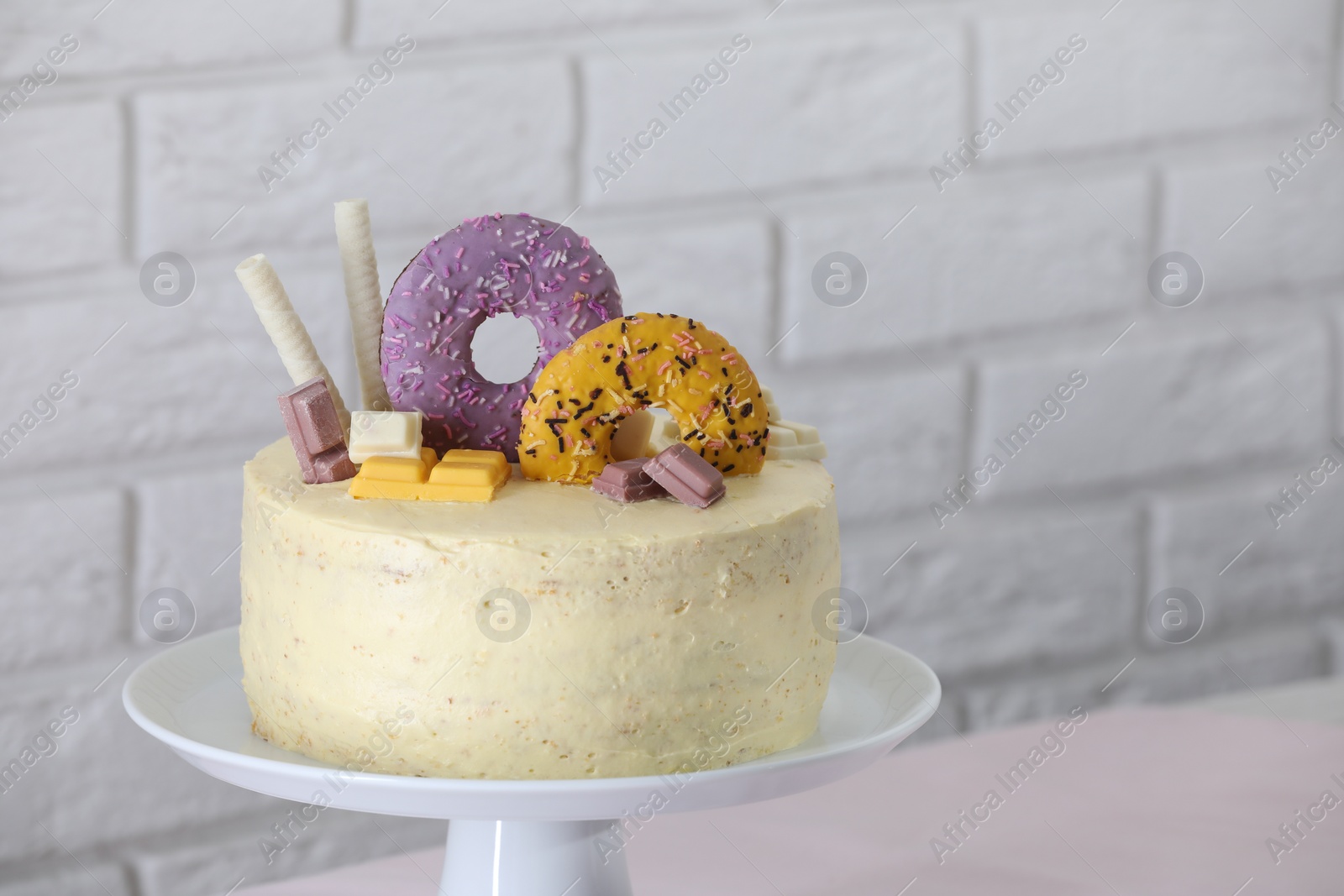 Photo of Delicious cake decorated with sweets on table near white brick wall, space for text