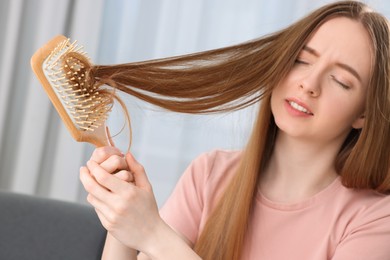 Photo of Upset woman brushing her hair at home, selective focus. Alopecia problem
