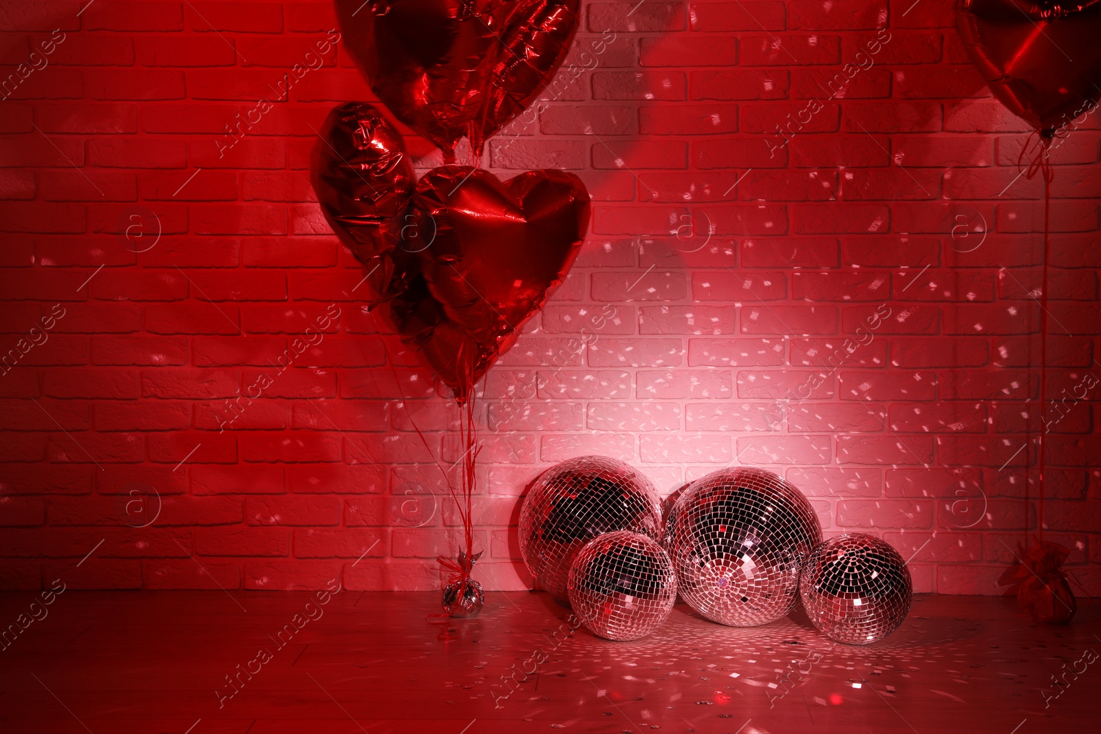 Photo of Many shiny disco balls in room decorated with heart shaped balloons, toned in red