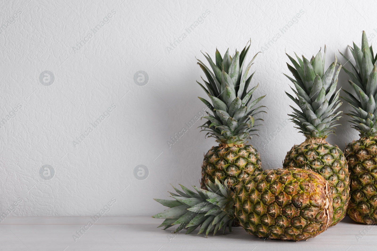 Photo of Whole ripe pineapples on white wooden table, space for text