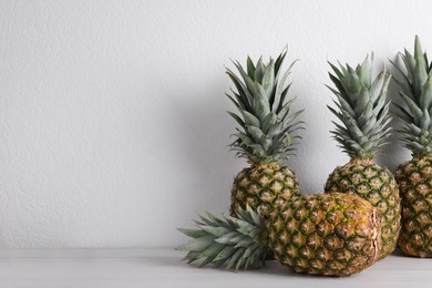 Photo of Whole ripe pineapples on white wooden table, space for text