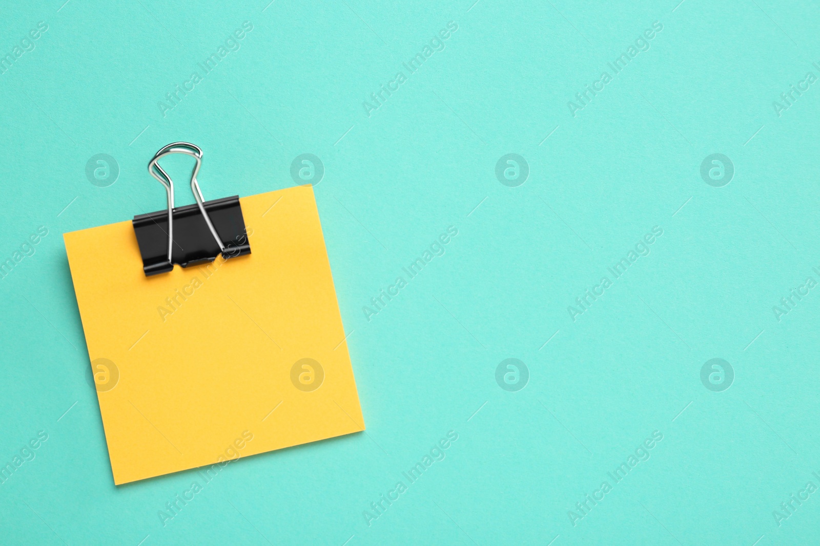 Photo of Blank orange note with black paper clamp on turquoise background, top view. Space for text