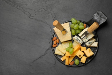 Photo of Cheese platter with specialized knife and fork on black table, top view. Space for text